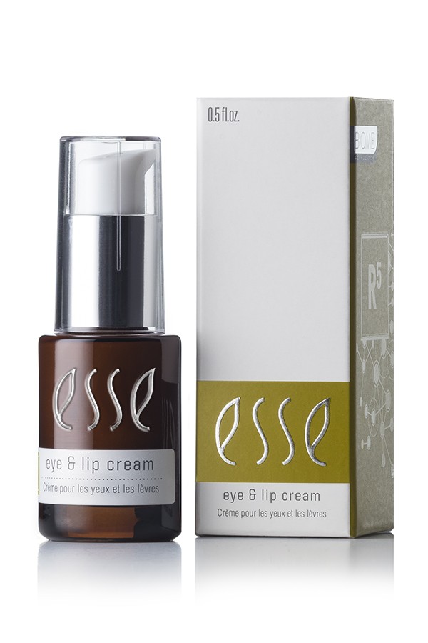 A small brown bottle of "Esse Eye & Lip Cream," featuring a pump dispenser, is placed beside its white and green packaging box. The packaging displays the text “eye & lip cream” along with the French translation “Crème pour les yeux et les lèvres,” and indicates a volume of 0.5 fl oz.
