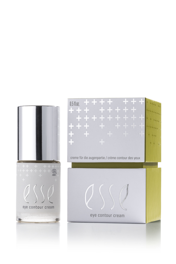 A small bottle of Esse Eye Contour Cream with a silver cap is placed beside its matching white and green box, which features silver cross patterns and product details in English and French.