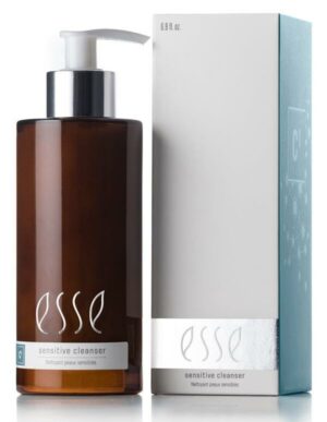 A dark brown bottle of Esse Sensitive Cleanser with a white pump dispenser is placed beside its light grey and teal packaging box. Both the bottle and the box are labeled as suitable for sensitive skin, with the bottle containing 6.8 fl. oz.